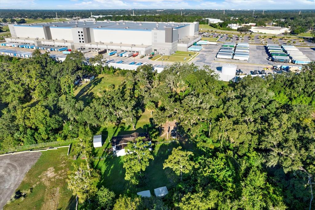 An aerial view shows a house nestled in trees next to a large industrial warehouse — 9211 HARNEY BAPTIST CHURCH ROAD, TAMPA, FL