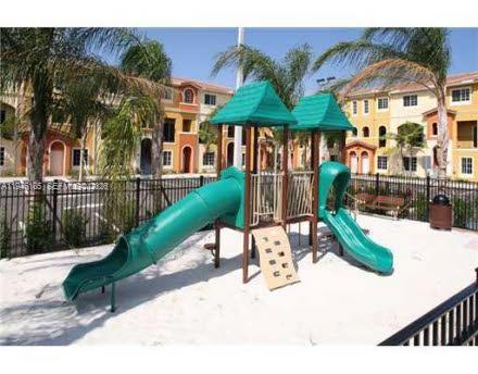 A playground with two green slides and two roofed towers sits on a sandy lot — 141 NW 2nd Ave # 7, Hallandale Beach FL 33009, HALLANDALE BEACH, FL