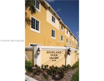 A low-angle view of a yellow multi-story building behind a wall labeled Highland Park Village — 141 NW 2nd Ave # 7, Hallandale Beach FL 33009, HALLANDALE BEACH, FL