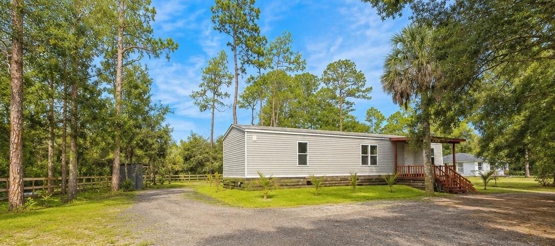 A single-story manufactured home with gray siding sits on a gravel lot among trees — 875 N Cabbage Palm Street, Clewiston FL 33440, CLEWISTON, FL