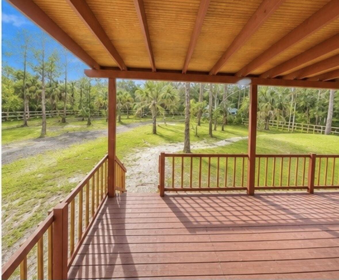 A wooden deck with a covered roof overlooks a grassy yard with trees and fencing — 875 N Cabbage Palm Street, Clewiston FL 33440, CLEWISTON, FL