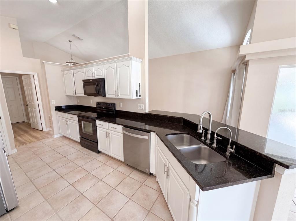 A kitchen features white cabinets, dark granite countertops, stainless steel appliances, and tile flooring — 1619 RIVER BIRCH AVENUE, OVIEDO, FL