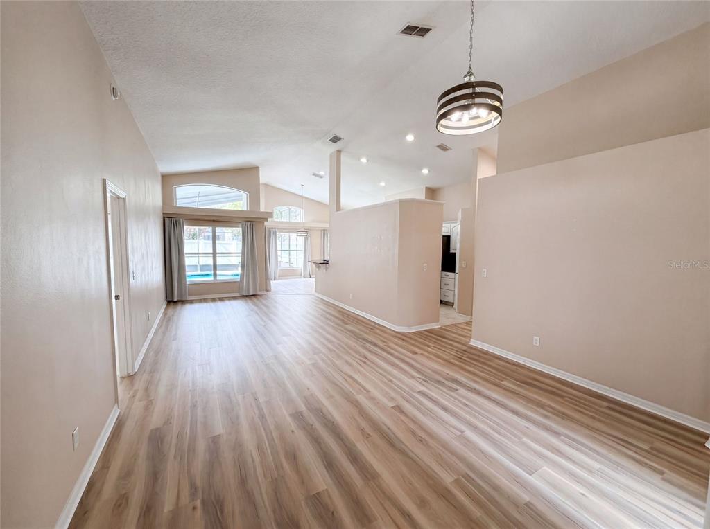 An open-concept living area features light wood-look flooring, vaulted ceilings, and a modern pendant light — 1619 RIVER BIRCH AVENUE, OVIEDO, FL