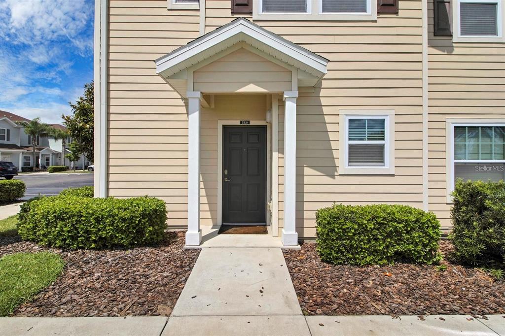 The exterior of a tan, two-story townhouse features a covered entryway with a dark door — 3221 CUPID PLACE, KISSIMMEE, FL