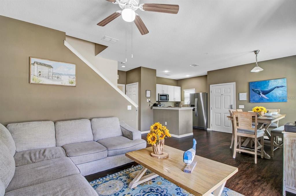 An open-concept living room and kitchen featuring a gray sectional, wood floors, and neutral walls — 3221 CUPID PLACE, KISSIMMEE, FL