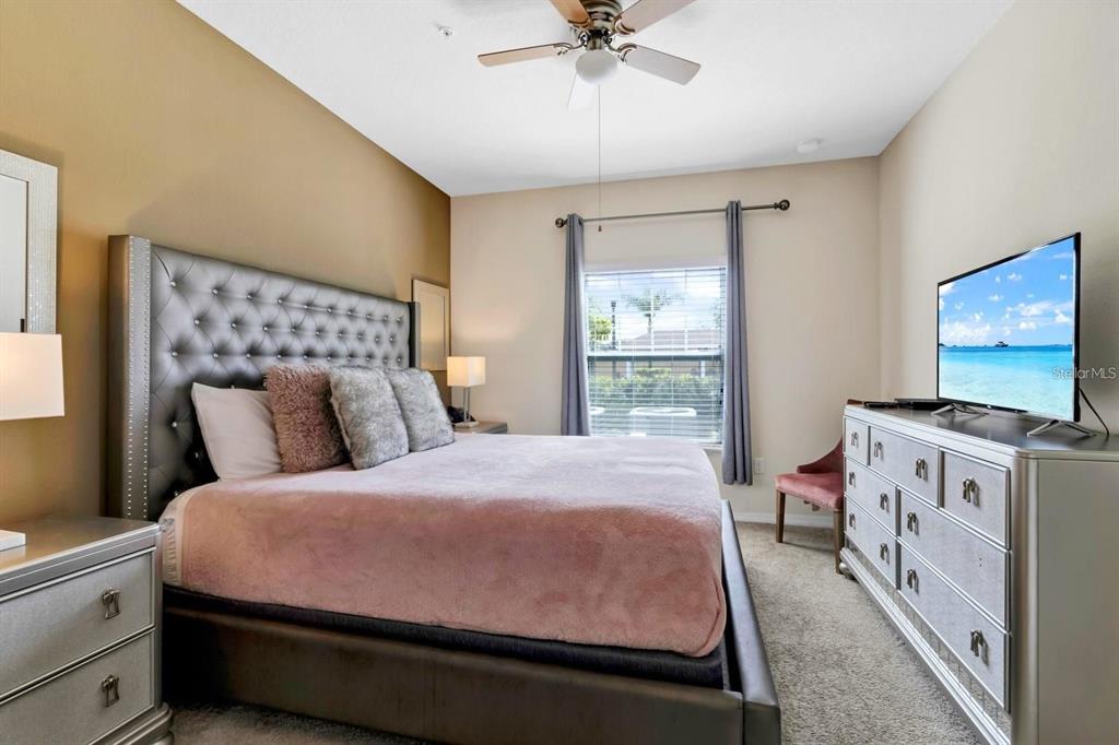 A bedroom features a tufted headboard, a pink bedspread, a dresser, and a ceiling fan — 3221 CUPID PLACE, KISSIMMEE, FL