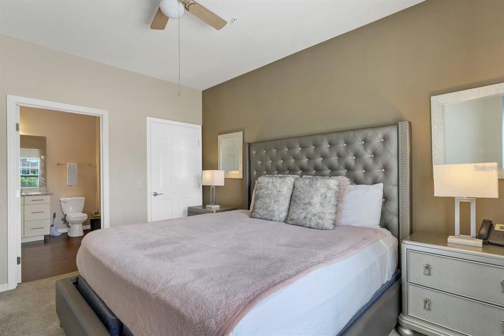A bedroom features a tufted gray headboard, a plush blanket, and an attached bathroom — 3221 CUPID PLACE, KISSIMMEE, FL