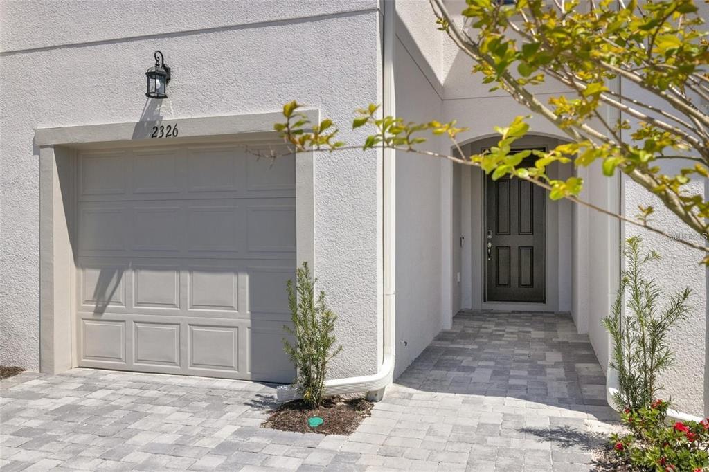 A beige stucco house exterior featuring a single-car garage, a dark front door, and pavers — 2326 SUMMERLIT STREET, LUTZ, FL
