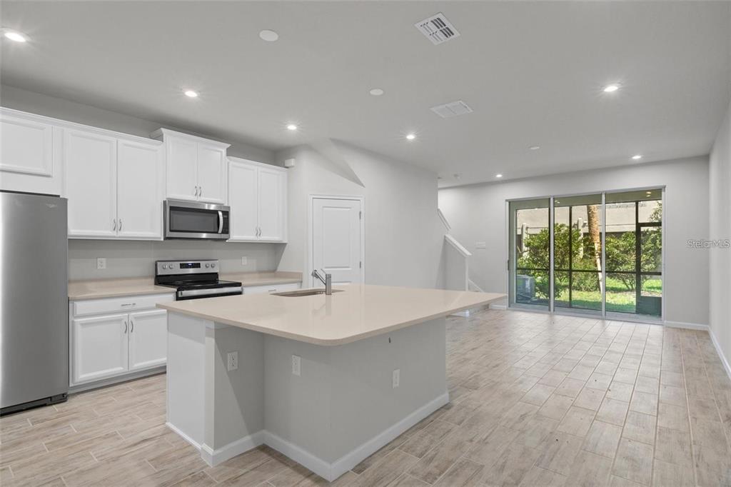 A modern kitchen with white cabinets, a quartz island, and tile flooring opens to a patio — 2326 SUMMERLIT STREET, LUTZ, FL