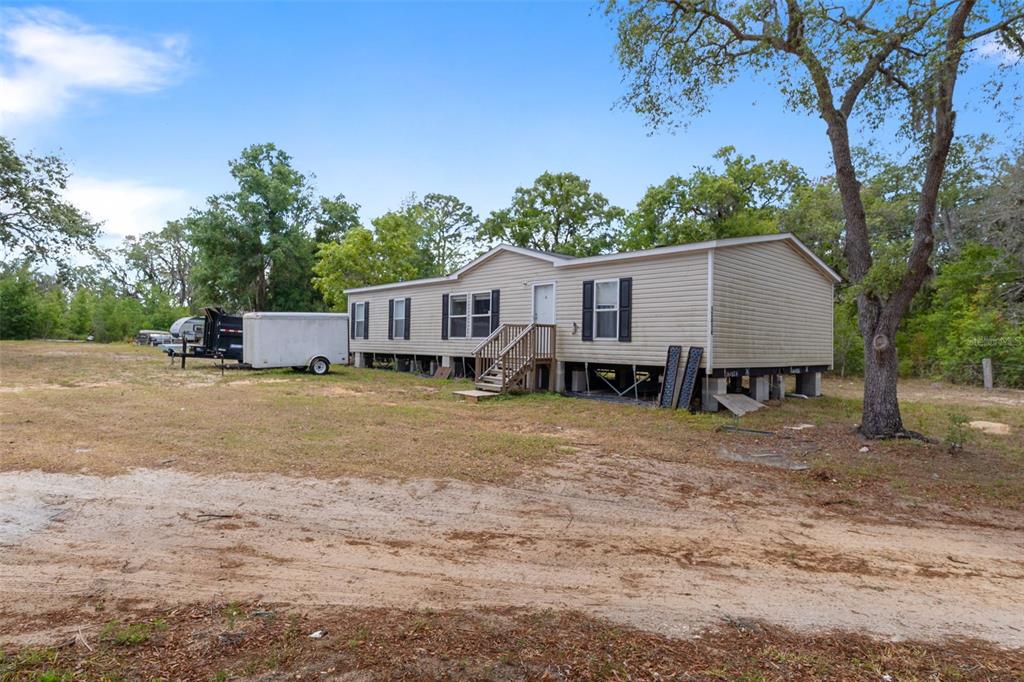 A single-story manufactured home sits on a dirt lot surrounded by trees and a trailer — 12434 CHOCTAW TRAIL, HUDSON, FL