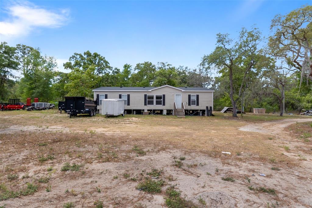 A tan manufactured home sits on a large, sandy lot surrounded by trees and trailers — 12434 CHOCTAW TRAIL, HUDSON, FL