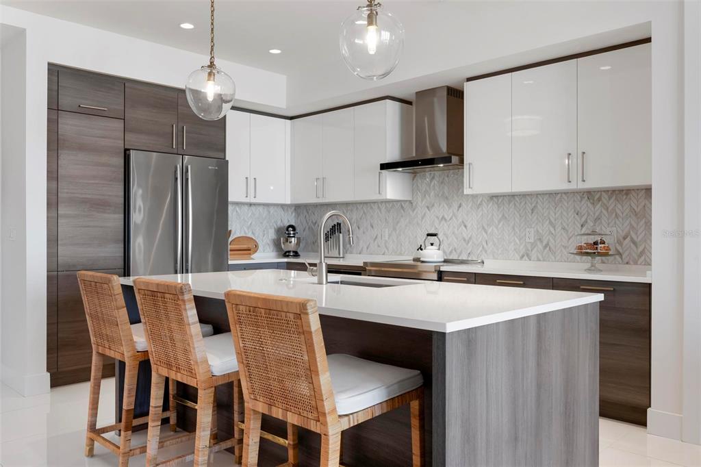 A modern kitchen features a large island with wicker stools, white cabinets, and wood-toned cabinetry — 111 S PINEAPPLE AVENUE UNIT 719, SARASOTA, FL