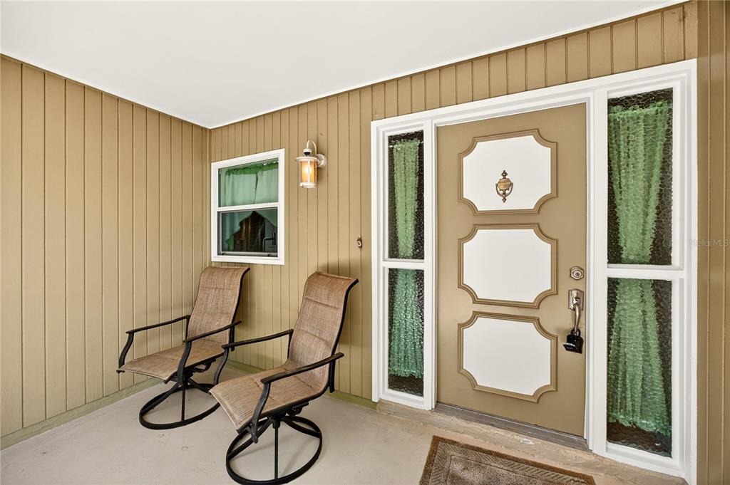 A covered porch features two chairs, a light fixture, and a front door with sidelights — 20 BLEAU COURT, PALM COAST, FL