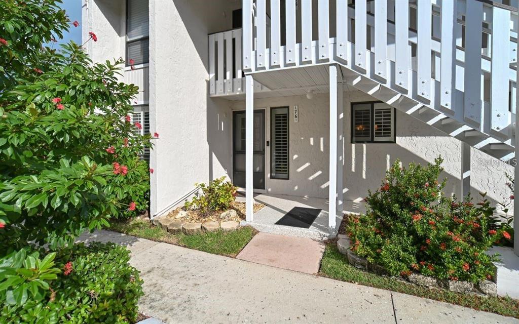 An exterior view of a ground-floor apartment entrance with a white staircase and landscaping — 1801 GULF DRIVE N UNIT 176, BRADENTON BEACH, FL