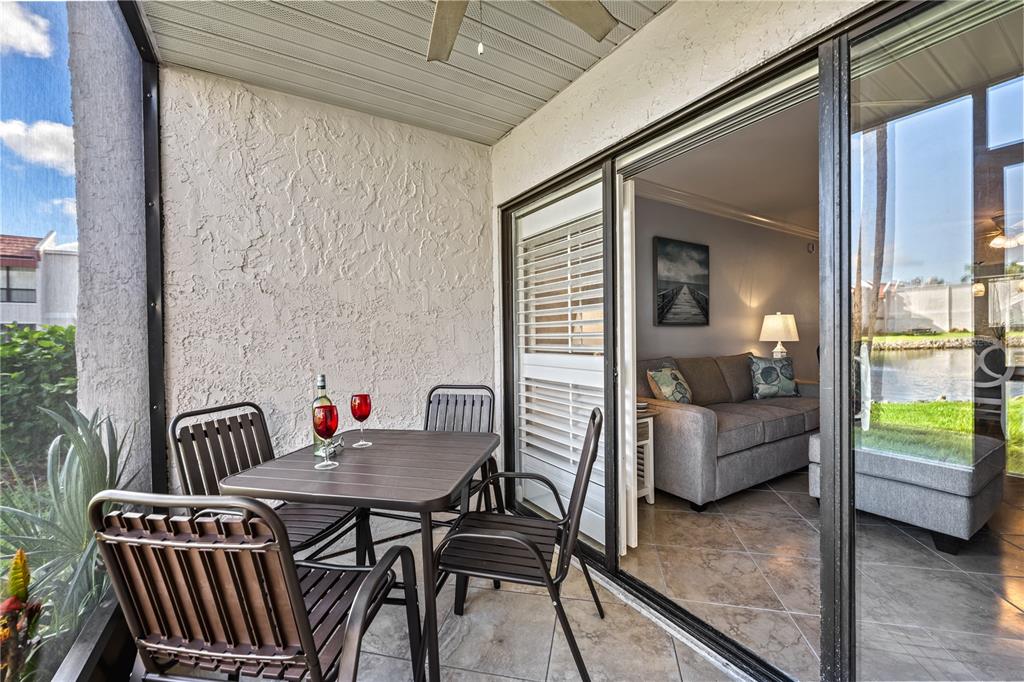 A screened-in patio with a dining set overlooks a lake through sliding glass doors — 1801 GULF DRIVE N UNIT 176, BRADENTON BEACH, FL