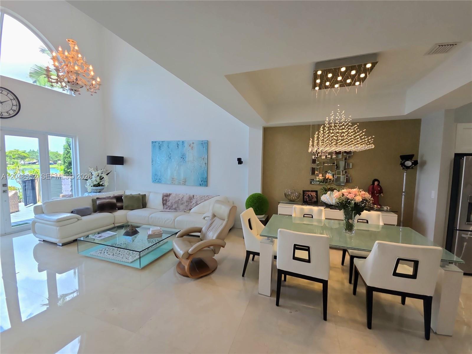 A bright, open-concept living and dining room features white tile floors and modern chandeliers — 783 NE 195th St # 0, Miami FL 33179, MIAMI, FL