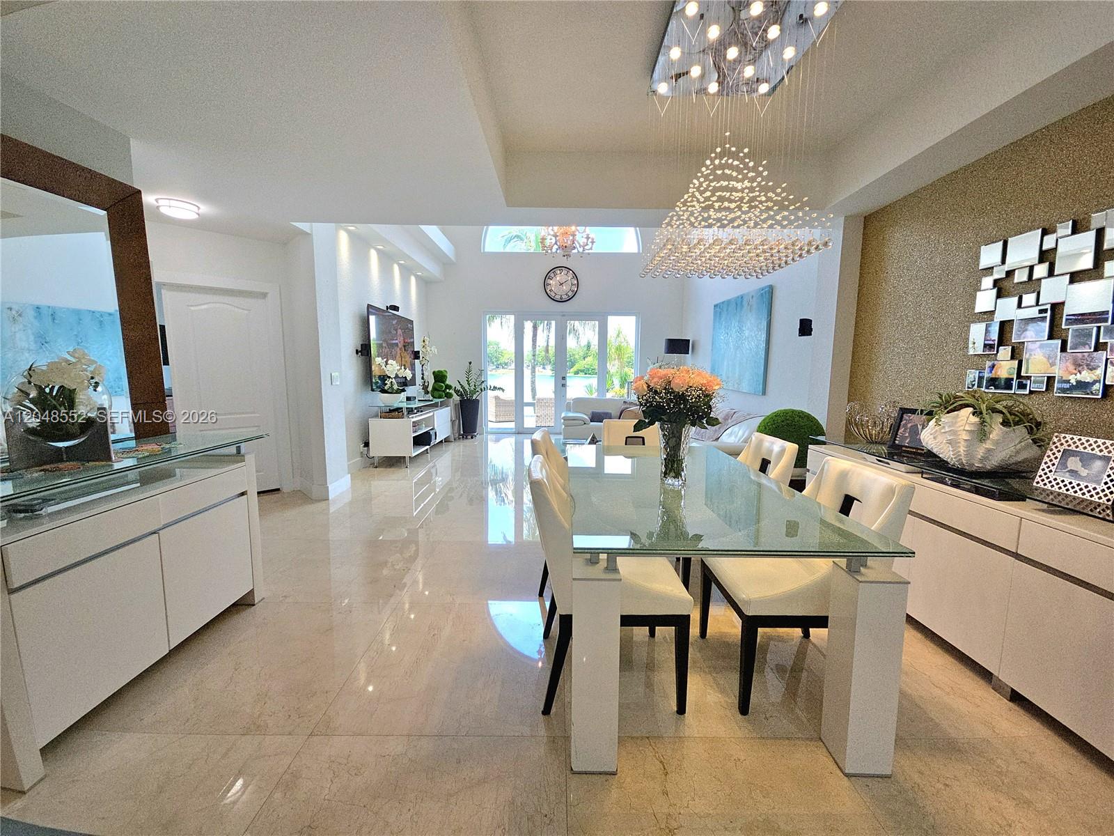 A modern dining room features a glass table, white chairs, and a large crystal chandelier — 783 NE 195th St # 0, Miami FL 33179, MIAMI, FL