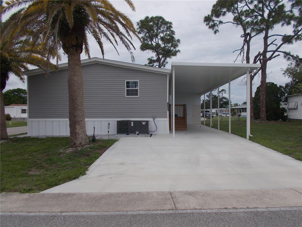 A gray manufactured home features a concrete driveway, a white carport, and a palm tree — 6803 AMOKO COURT, NORTH PORT, FL