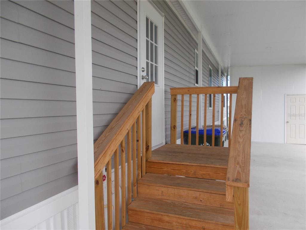 A wooden staircase with railings leads to a white door on a gray-sided home — 6803 AMOKO COURT, NORTH PORT, FL