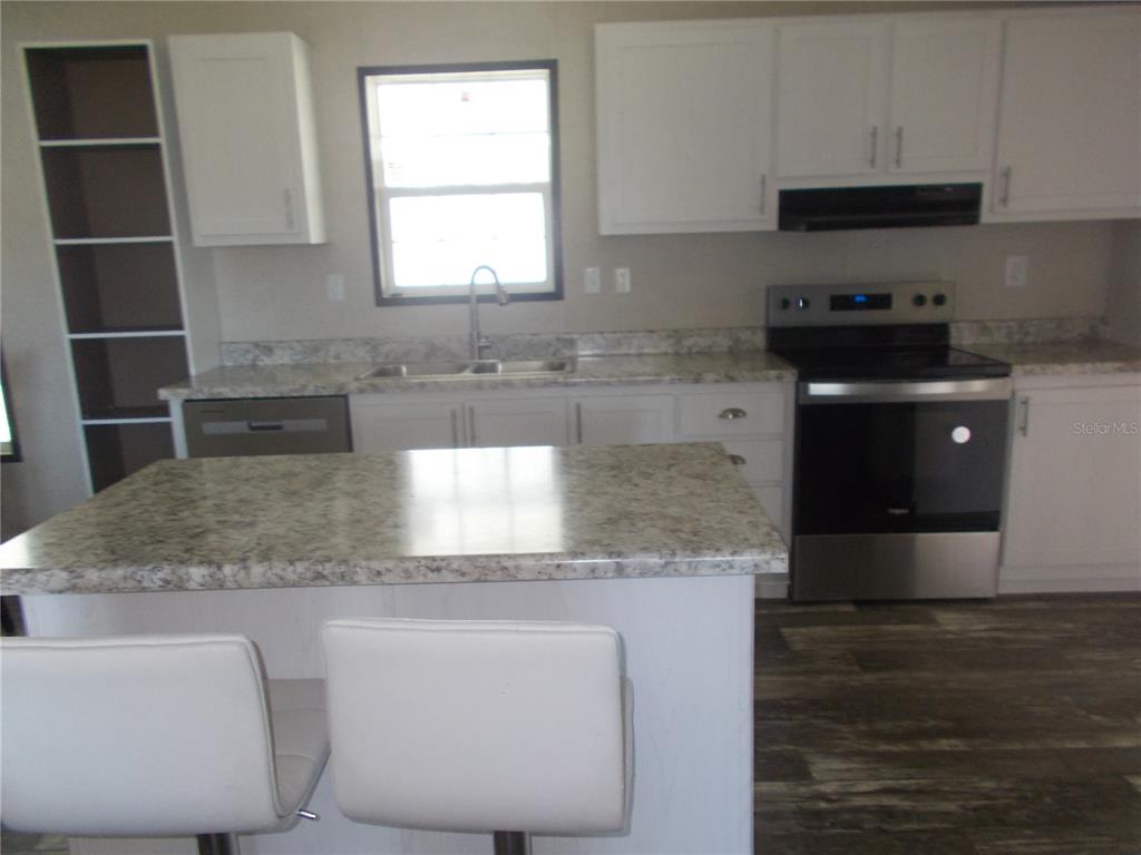 A kitchen features white cabinets, granite-look countertops, stainless steel appliances, and a central island — 6803 AMOKO COURT, NORTH PORT, FL