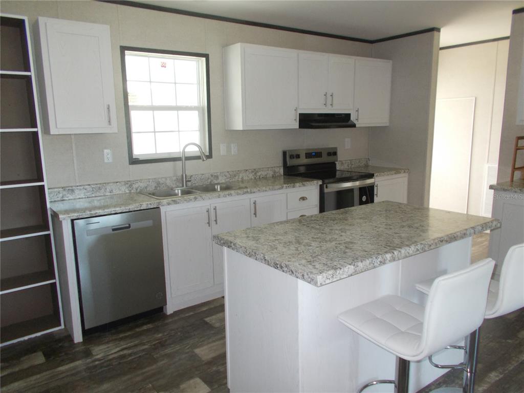 A kitchen features white cabinets, granite countertops, a stainless steel dishwasher, and a center island — 6803 AMOKO COURT, NORTH PORT, FL