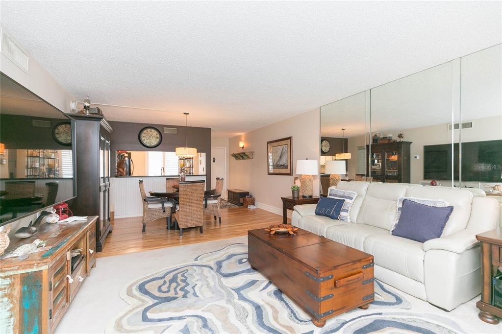 A living room and dining area with hardwood floors, a white sofa, and mirrored walls — 5510 PUERTA DEL SOL BOULEVARD S UNIT 232, ST PETERSBURG, FL