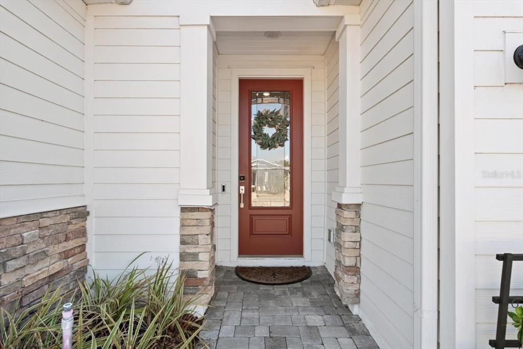 A red front door with a glass panel is framed by white siding and stone — 700 STILLWATER BOULEVARD, ST JOHNS, FL