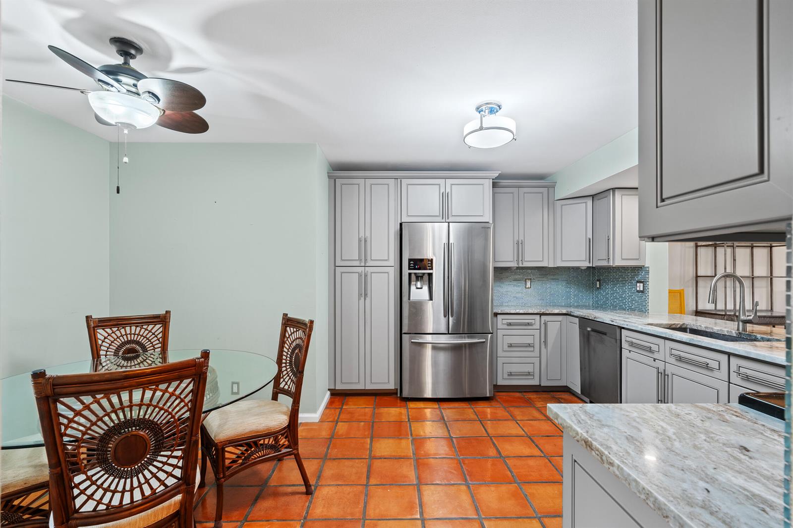 A kitchen and dining area features gray cabinets, stainless steel appliances, and terracotta tile flooring — 9728 Sills Drive E # 102, Boynton Beach FL 33437, BOYNTON BEACH, FL