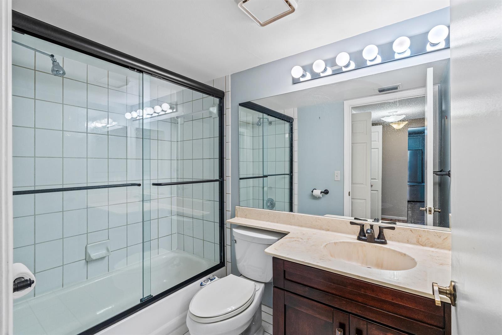 A bathroom features a shower-tub combo, a dark wood vanity, and a large wall mirror — 9728 Sills Drive E # 102, Boynton Beach FL 33437, BOYNTON BEACH, FL
