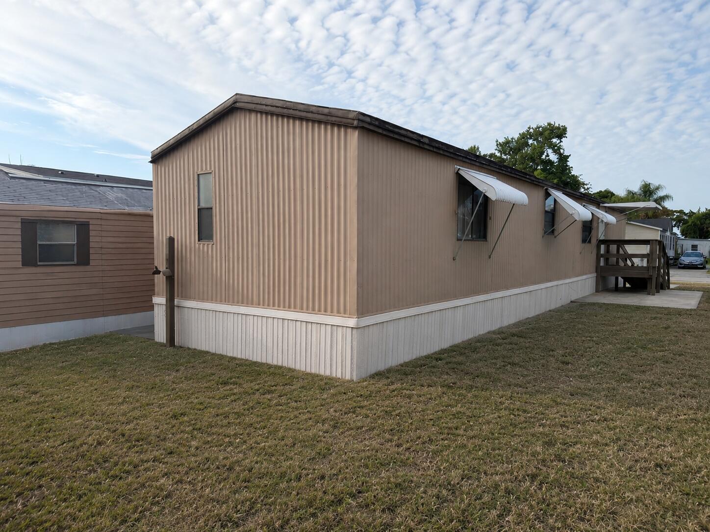 The exterior of a tan mobile home features vertical siding, white skirting, and window awnings — 2547 Chatham Way NE, Palm Bay FL 32905, PALM BAY, FL