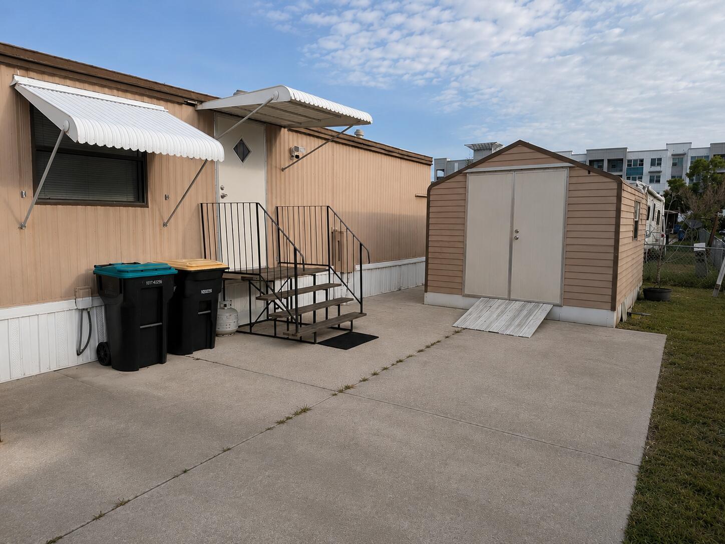 A mobile home with a concrete patio, metal stairs, and a detached storage shed — 2547 Chatham Way NE, Palm Bay FL 32905, PALM BAY, FL