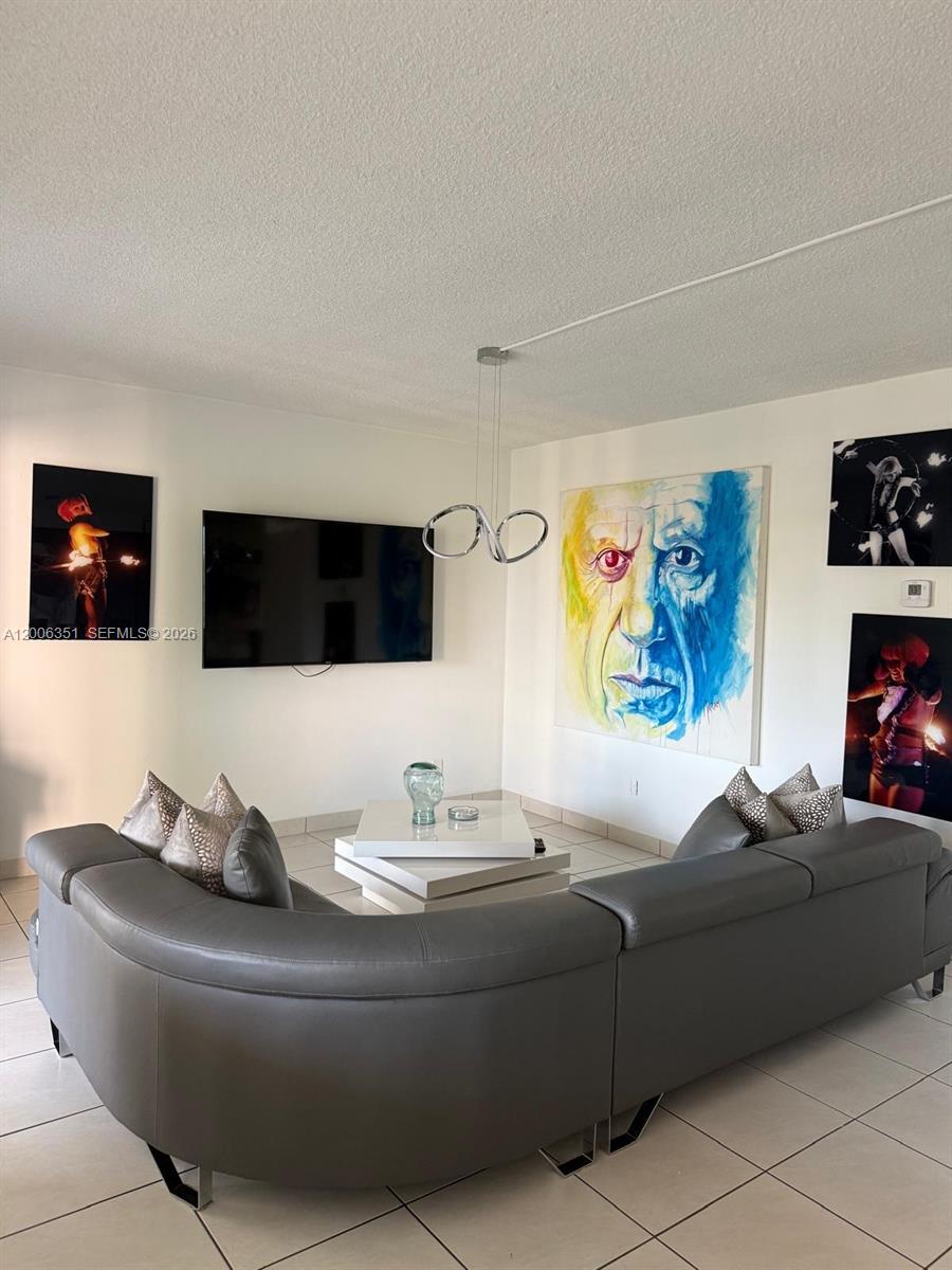 A living room features a grey sectional sofa, a wall-mounted television, and large wall art — 200 NE 12th Ave # 7E, Hallandale Beach FL 33009, HALLANDALE BEACH, FL