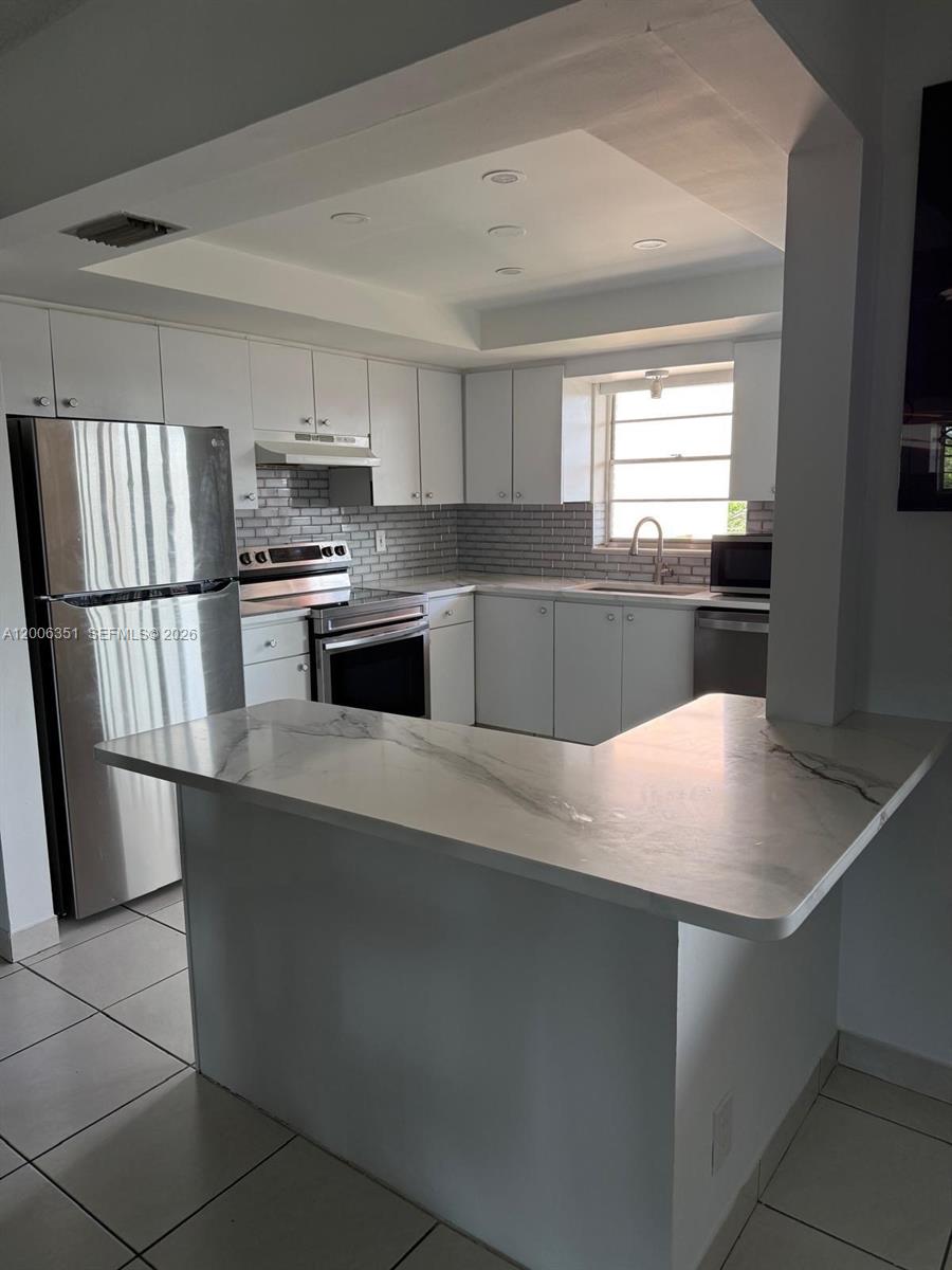 A kitchen features white cabinets, stainless steel appliances, a gray subway tile backsplash, and countertops — 200 NE 12th Ave # 7E, Hallandale Beach FL 33009, HALLANDALE BEACH, FL