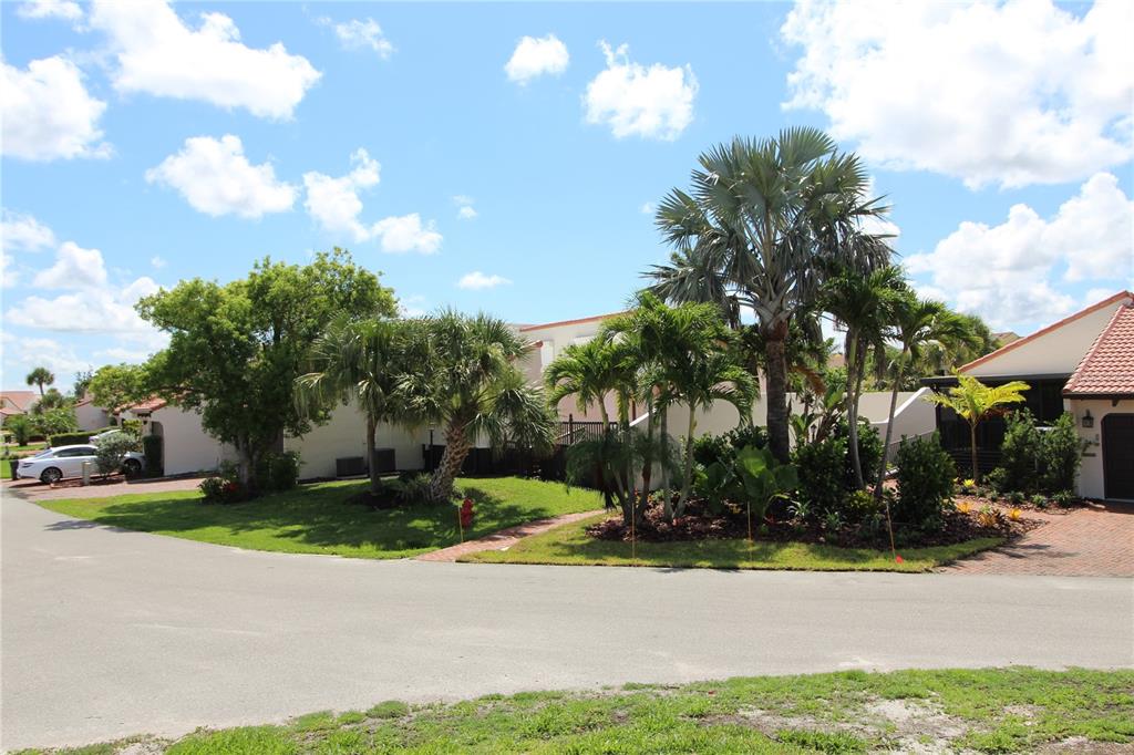 A residential street view featuring palm trees, landscaping, and a white car parked near houses — 25188 MARION AVENUE UNIT 24, PUNTA GORDA, FL
