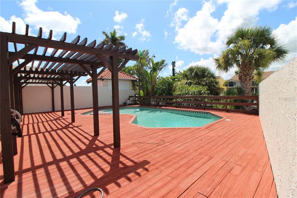 A wooden deck with a pergola overlooks a swimming pool in a fenced backyard — 25188 MARION AVENUE UNIT 24, PUNTA GORDA, FL