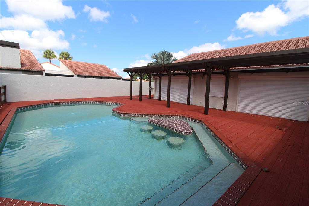 A swimming pool with in-pool seating sits beside a red deck and a covered patio — 25188 MARION AVENUE UNIT 24, PUNTA GORDA, FL