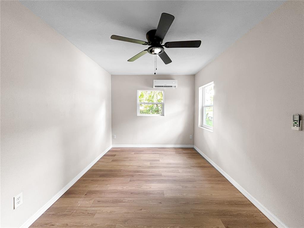 An empty room with light-colored walls, wood-look flooring, a ceiling fan, and a wall-mounted AC — 306 SW 19TH AVENUE, OCALA, FL