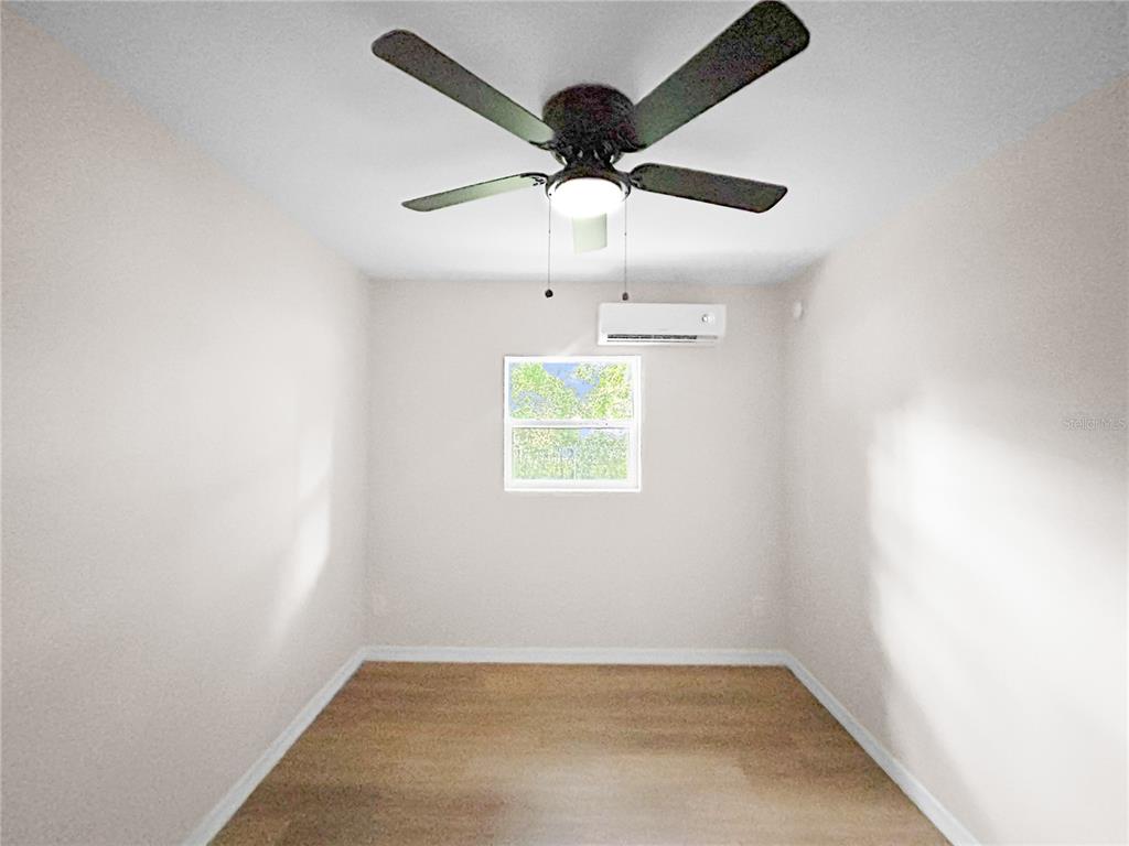 An empty room features light-colored walls, wood-look flooring, a ceiling fan, and a wall-mounted air conditioner — 306 SW 19TH AVENUE, OCALA, FL