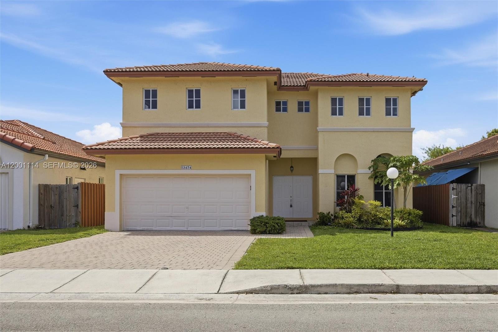 A two-story yellow stucco house features a tile roof, a two-car garage, and a lawn — 13474 SW 124th Ave Rd, Miami FL 33186, MIAMI, FL