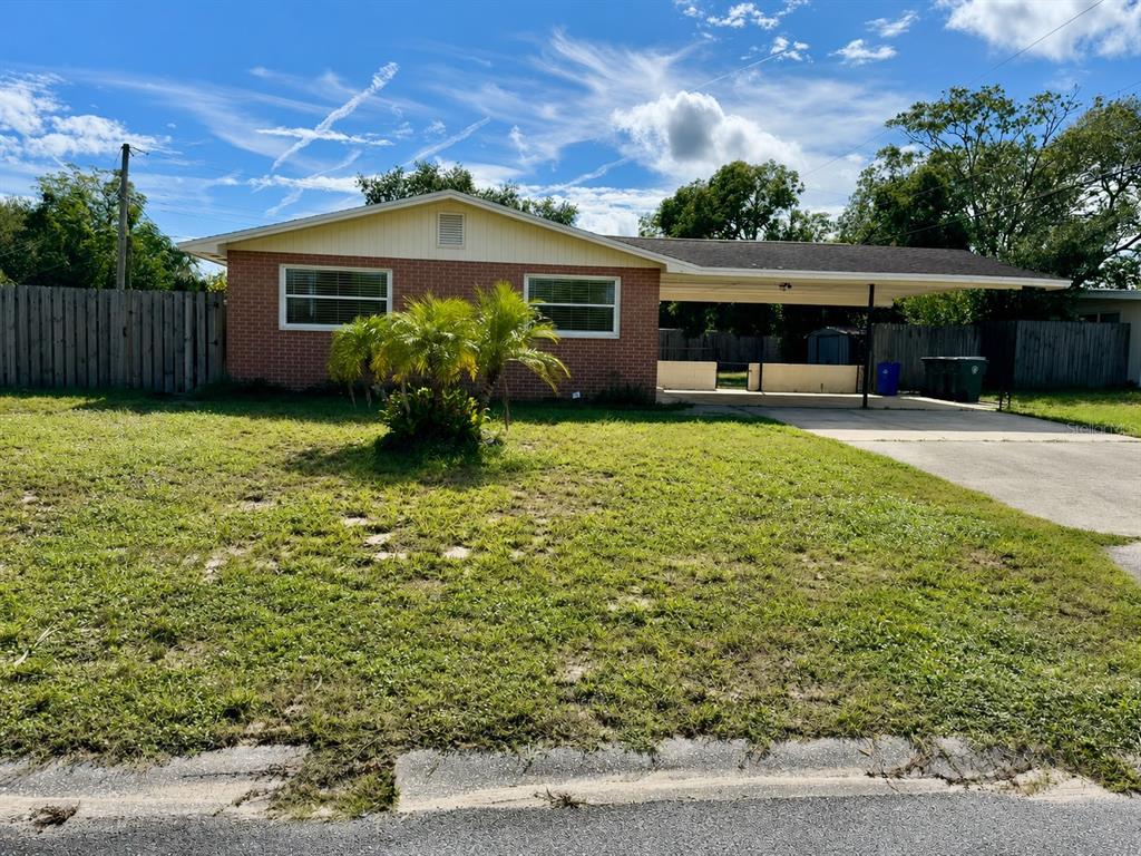 A single-story brick house with a carport and a fenced yard under a blue sky — 845 EDGEWOOD ROAD, TITUSVILLE, FL