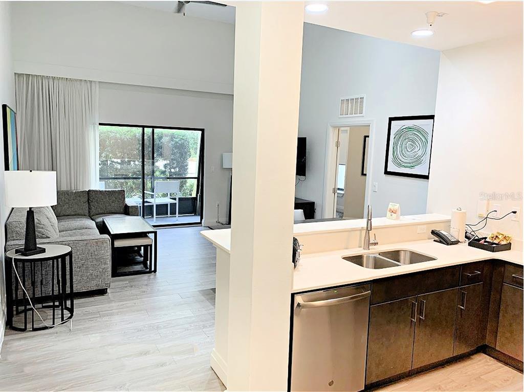 A kitchen with dark cabinets and a stainless dishwasher overlooks a living room with balcony — 14501 GROVE RESORT AVENUE UNIT 3109, WINTER GARDEN, FL