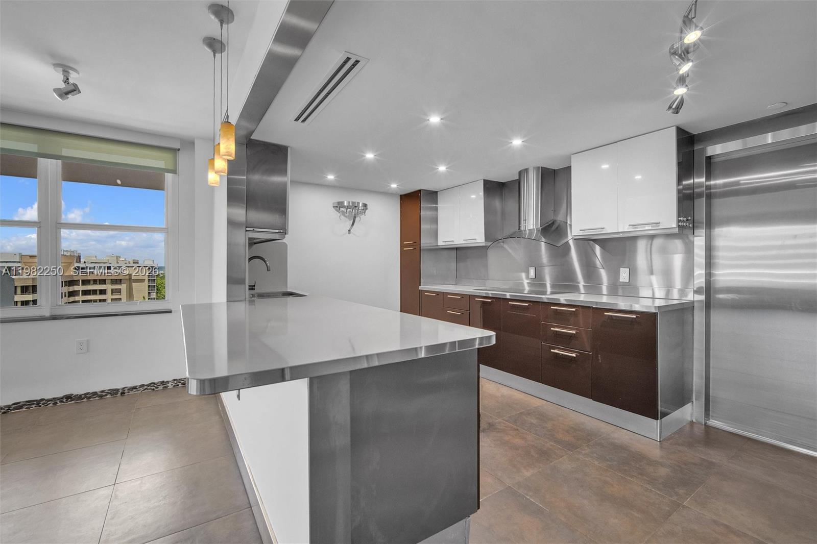 A modern kitchen features stainless steel surfaces, dark brown cabinetry, and a white breakfast bar — 199 Ocean Lane Dr # 1009, Key Biscayne FL 33149, KEY BISCAYNE, FL