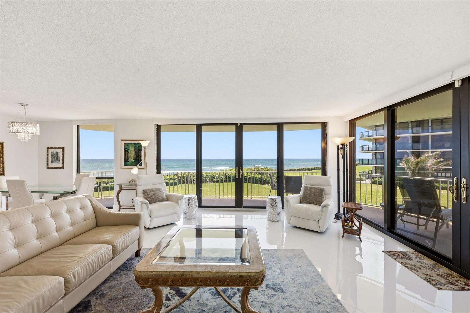 A living room with white tile floors, a leather sofa, and sliding doors overlooking the ocean — 3400 S Ocean Boulevard, Palm Beach FL 33480, PALM BEACH, FL