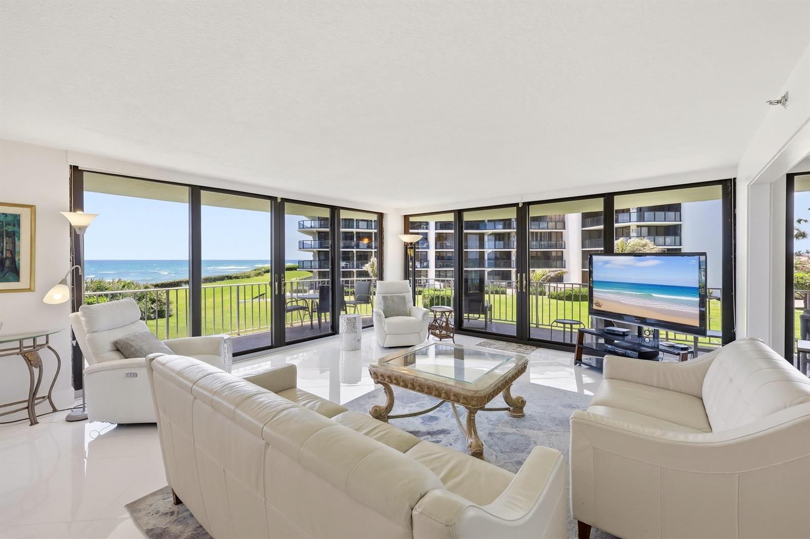 A bright living room with white leather furniture, a glass coffee table, and floor-to-ceiling windows — 3400 S Ocean Boulevard, Palm Beach FL 33480, PALM BEACH, FL