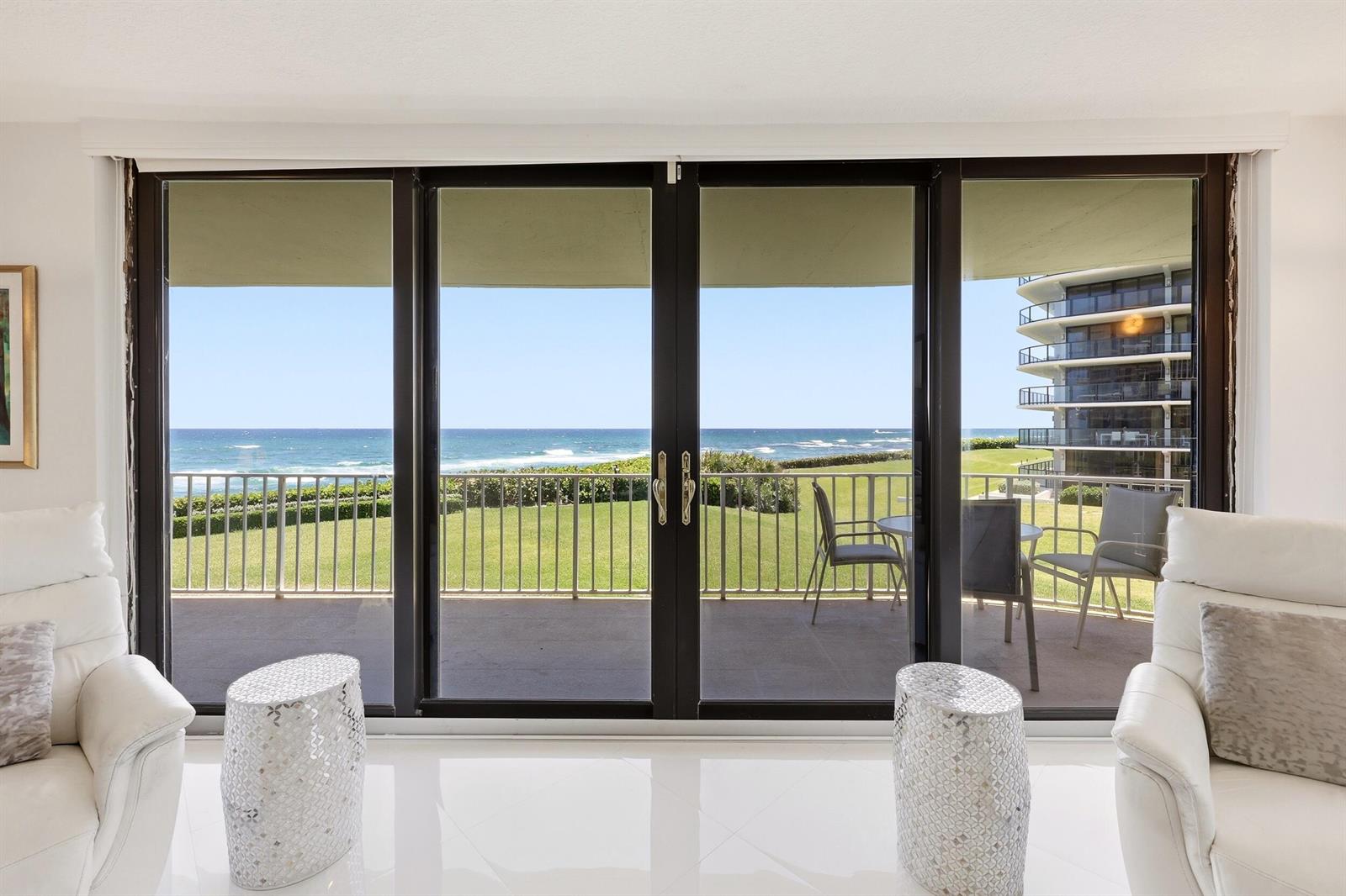 A living room with white leather chairs and a sliding glass door overlooking the ocean — 3400 S Ocean Boulevard, Palm Beach FL 33480, PALM BEACH, FL