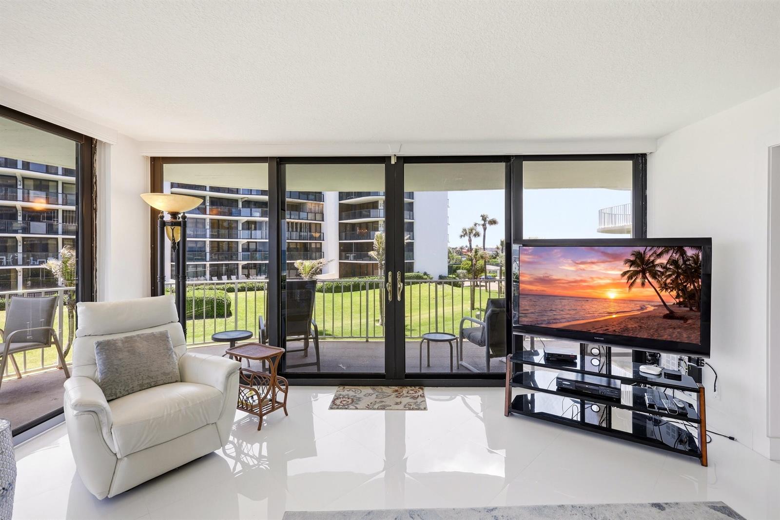 A living room features white tile floors, a white leather armchair, and sliding glass balcony doors — 3400 S Ocean Boulevard, Palm Beach FL 33480, PALM BEACH, FL