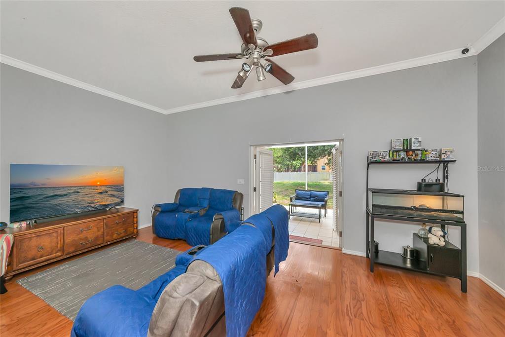 A living room features wood flooring, blue-covered furniture, a television, and a glass door to a patio — 11851 69TH STREET E, PARRISH, FL