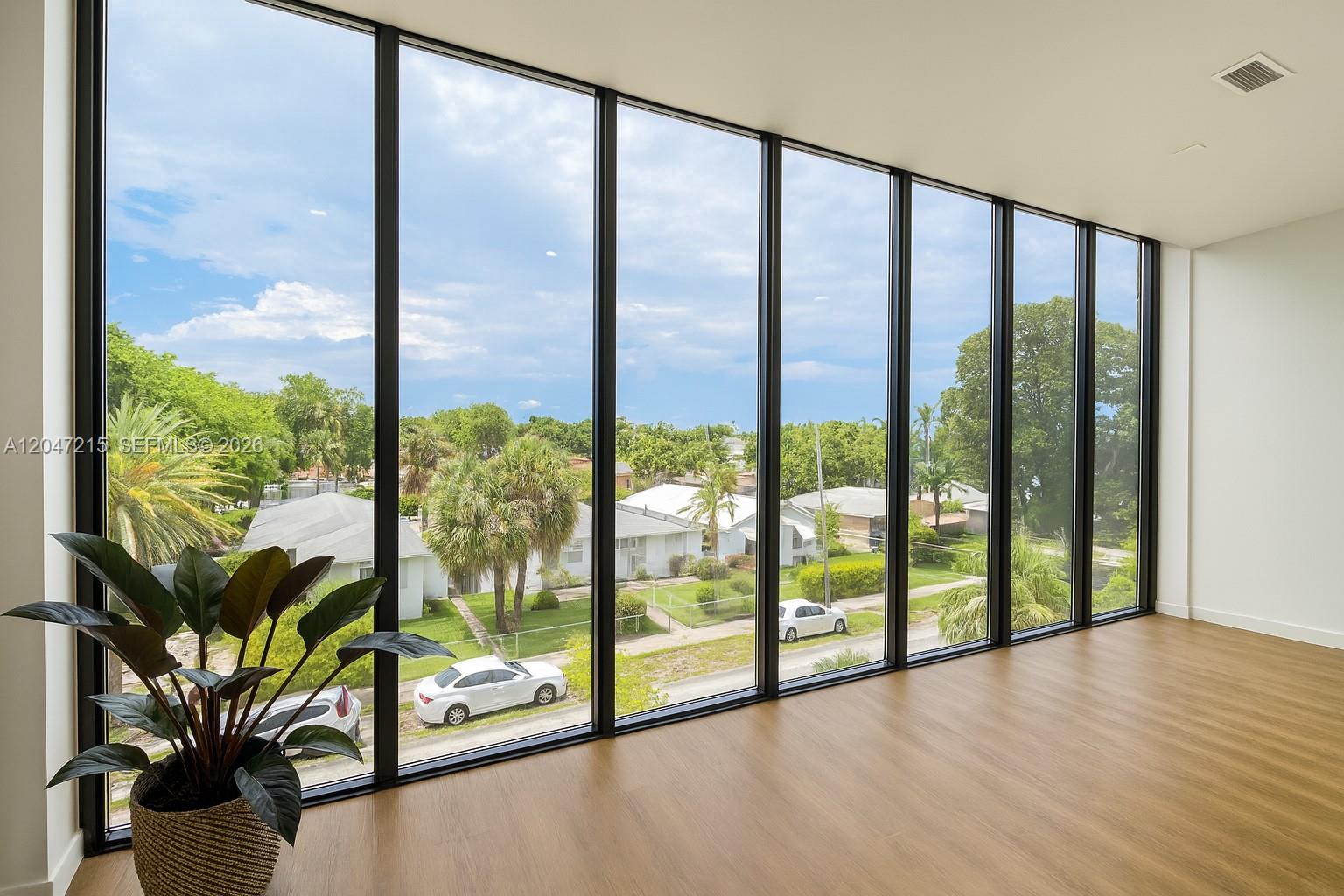 A room with floor-to-ceiling windows, wood-look flooring, and a potted plant overlooking a neighborhood — 1950 Fletcher St # 305, Hollywood FL 33020, HOLLYWOOD, FL