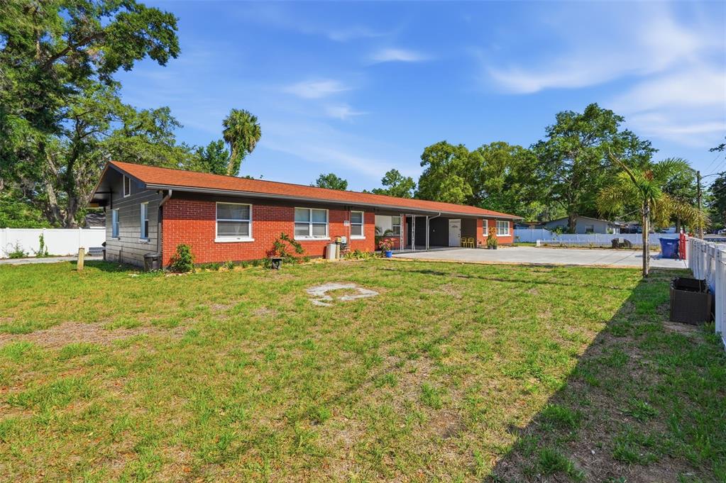 A single-story brick house with a large concrete driveway and a grassy backyard — 10107 N ASTER AVENUE, TAMPA, FL