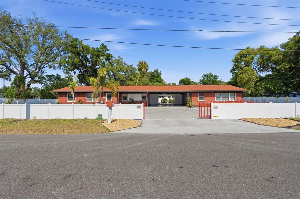 A single-story brick building with a central carport and white vinyl fencing — 10107 N ASTER AVENUE, TAMPA, FL